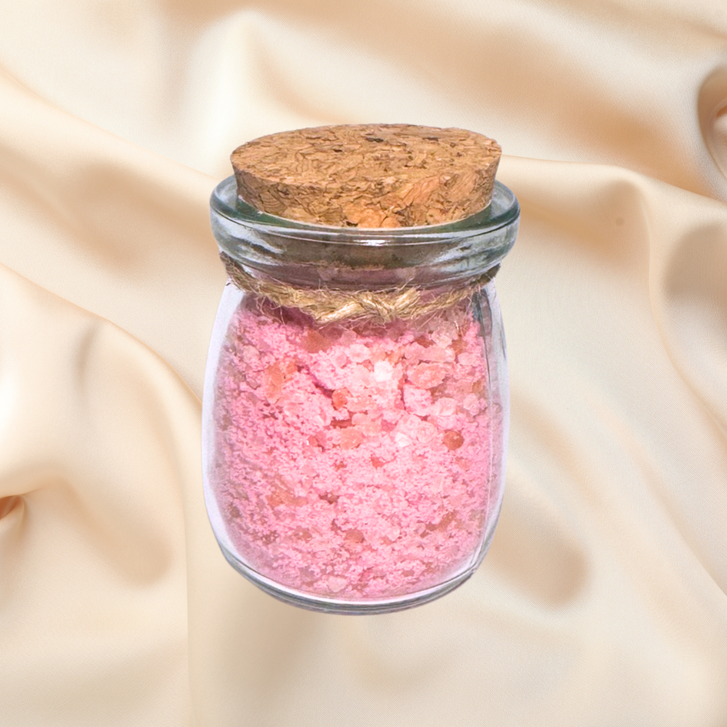 Glass jar with pink bath salts and cork lid on a beige fabric background