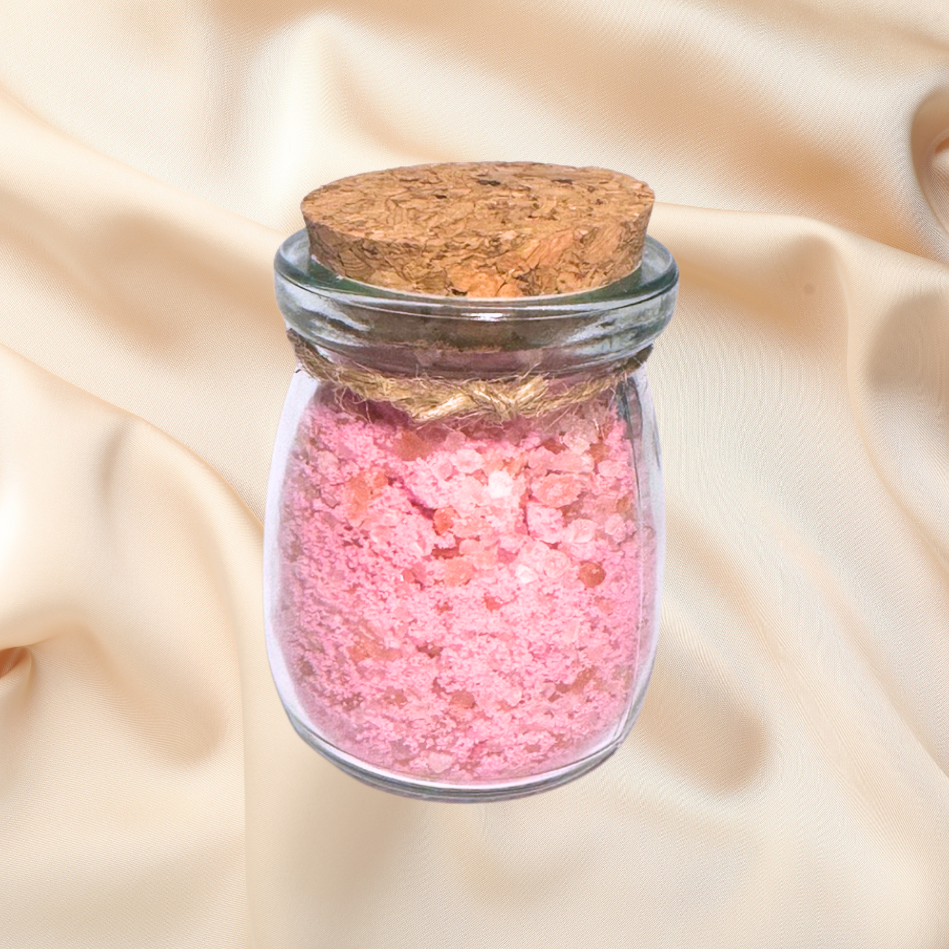 Glass jar with pink bath salts and cork lid on a beige fabric background