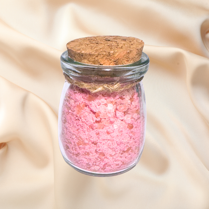 Glass jar with pink bath salts and cork lid on a beige fabric background