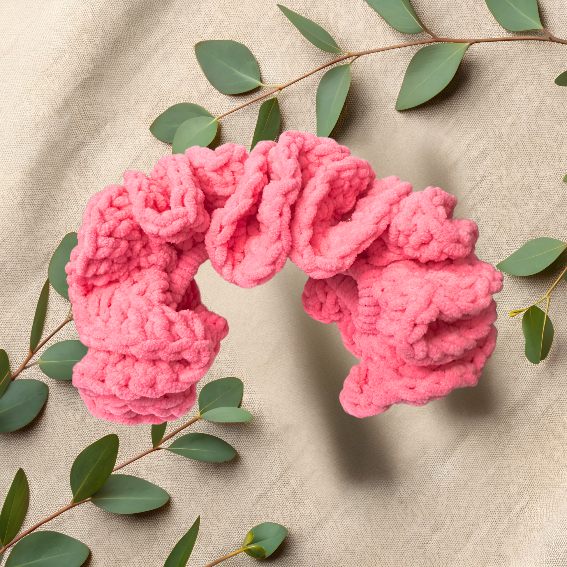 Pink knitted headband on a beige fabric background with green leaves.