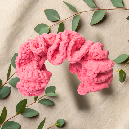 Pink knitted headband on a beige fabric background with green leaves.