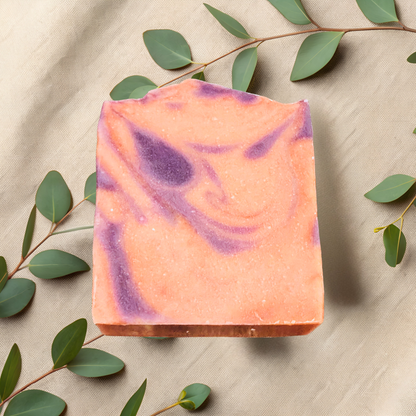 Swirled pink and purple soap bar on a beige fabric background with green leaves.