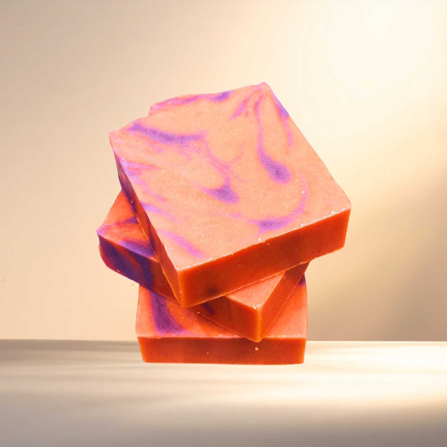 Stack of pink and orange marbled soap bars on a neutral background