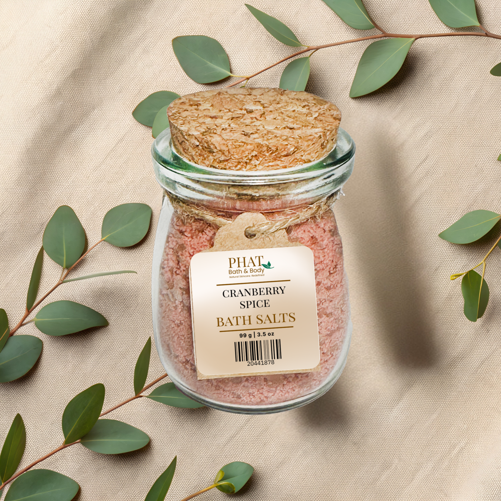 Jar of cranberry spice bath salts with a cork lid on a beige fabric background with green leaves.