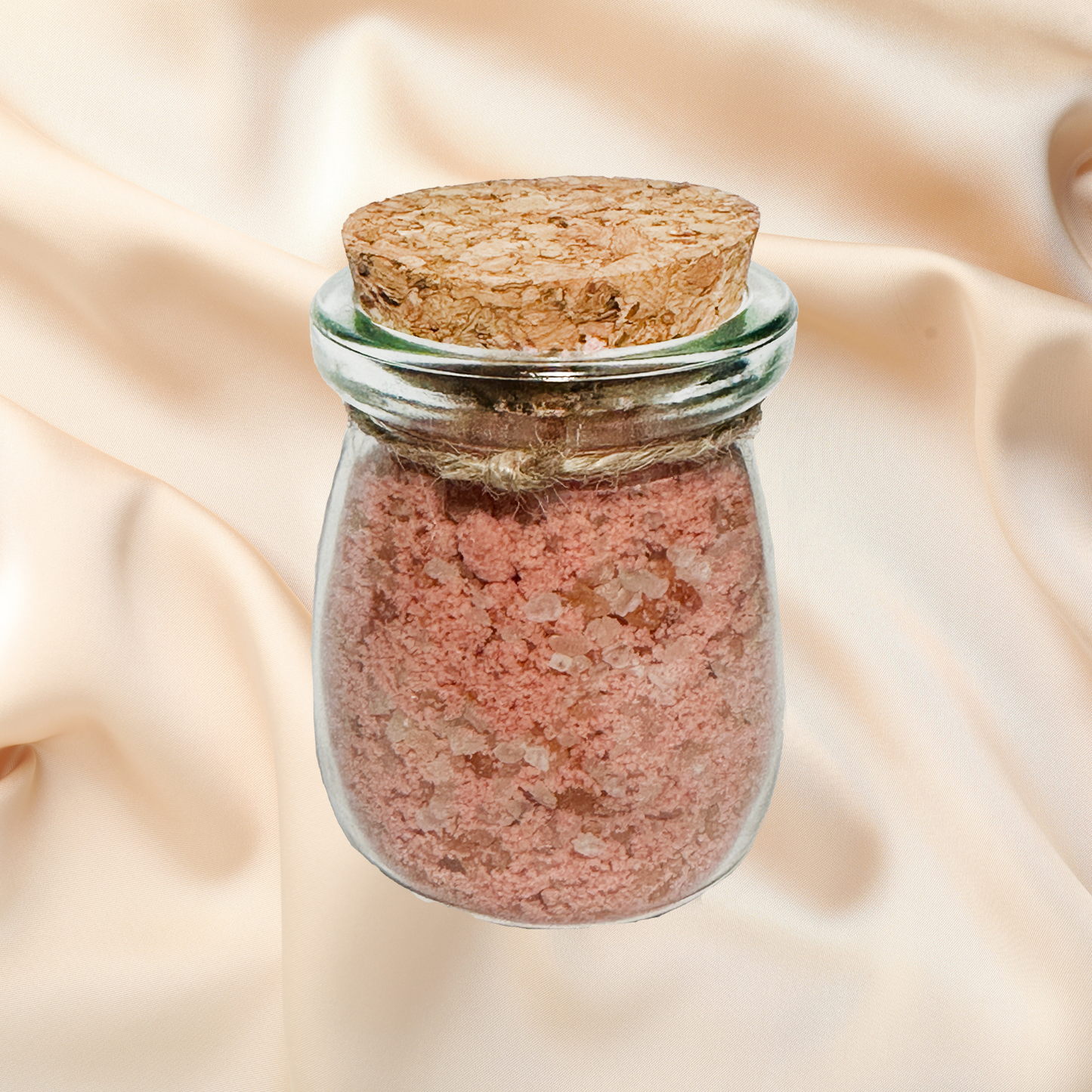 Glass jar with cork lid containing orange bath salts on a beige fabric background