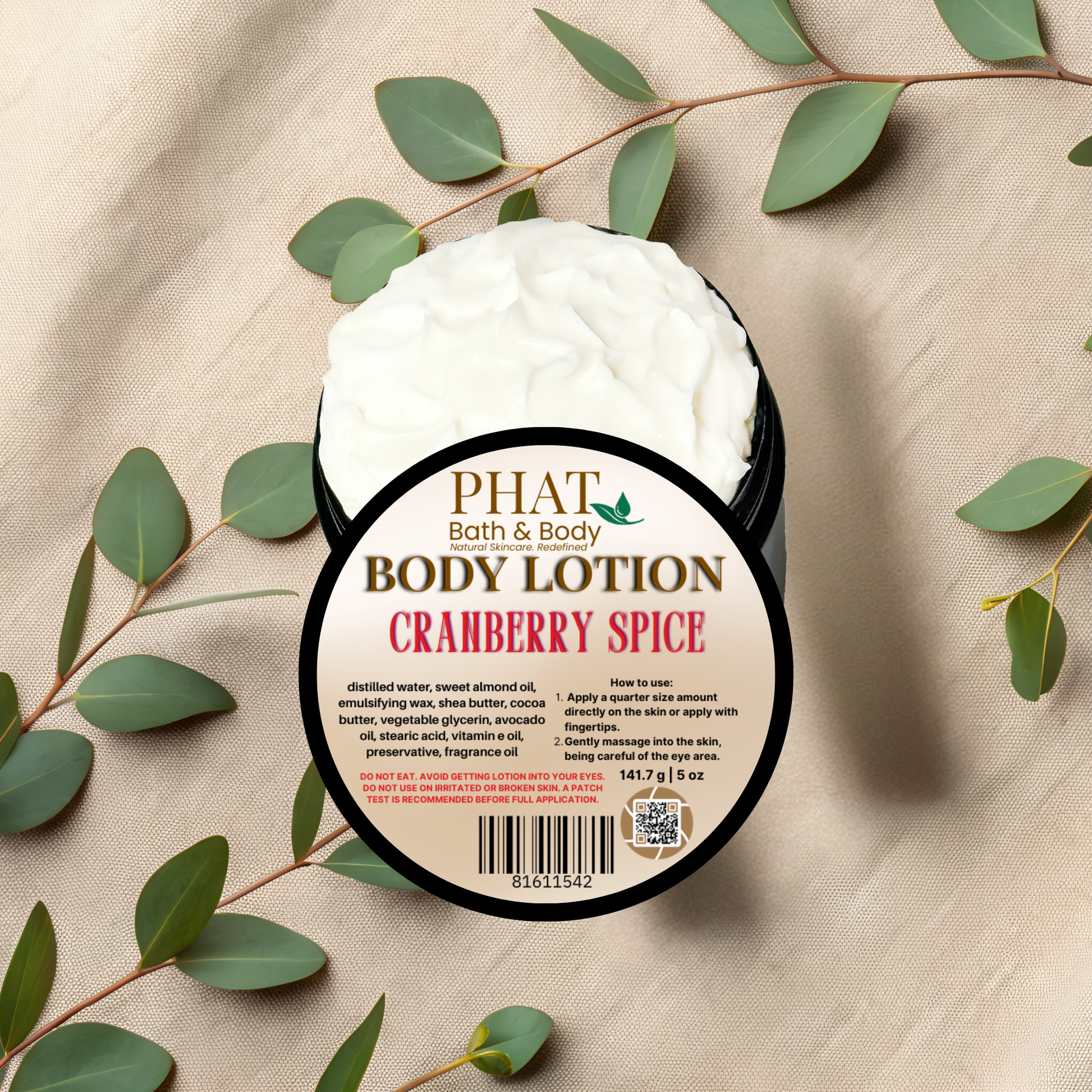 Body lotion container labeled 'Cranberry Spice' by Phat Bath & Body on a beige fabric background with green leaves.