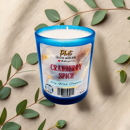 Cranberry Spice candle with a blue container on a beige fabric background with green leaves.