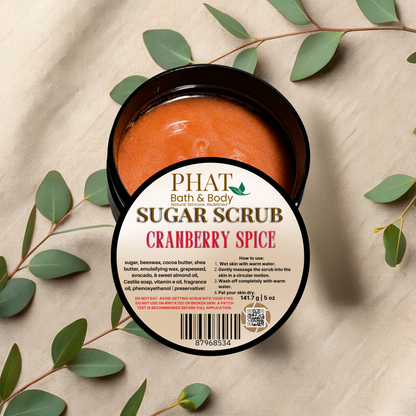 Cranberry Spice sugar scrub in a black container with a label on a beige fabric background with green leaves.