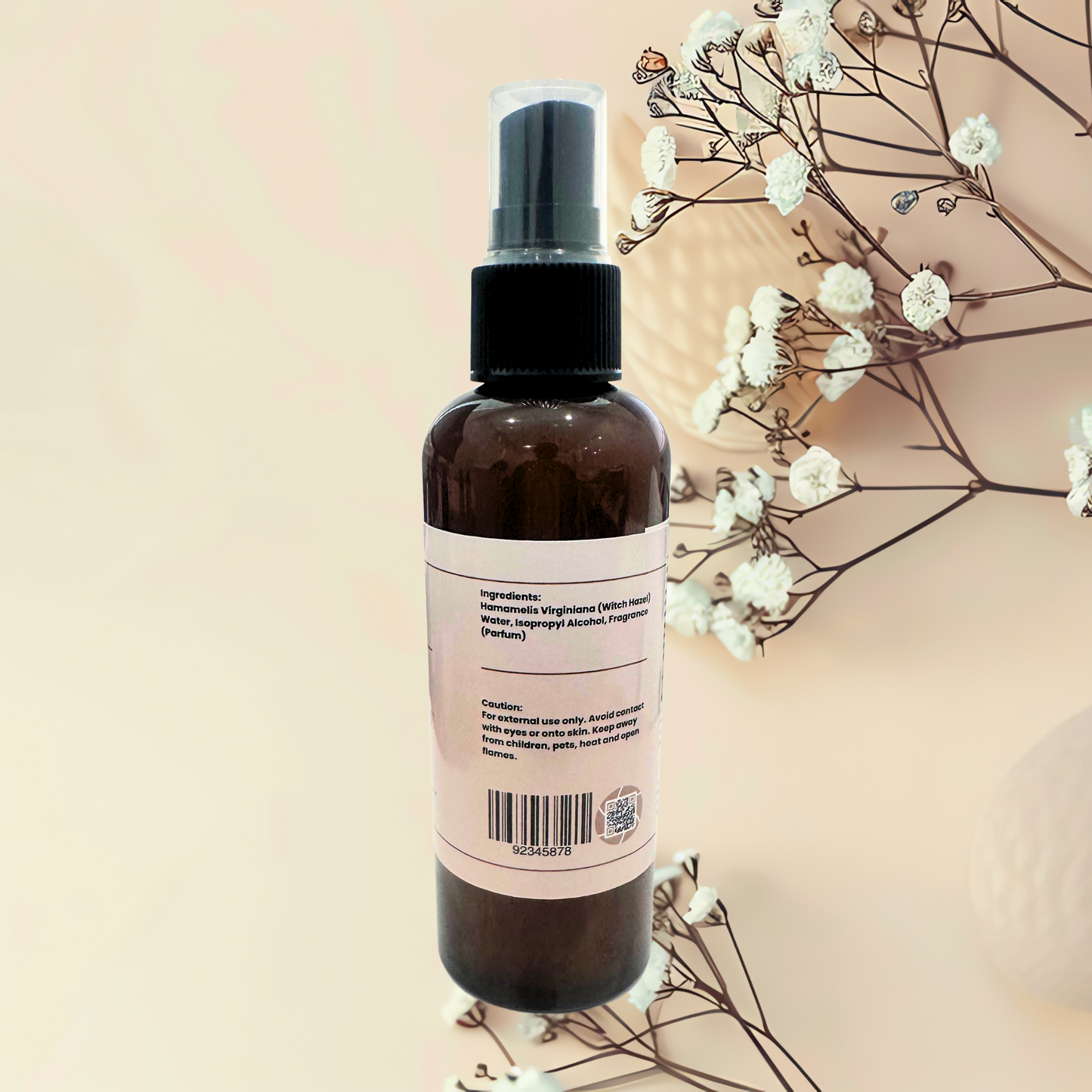 Brown spray bottle with a label on a beige background with white flowers.