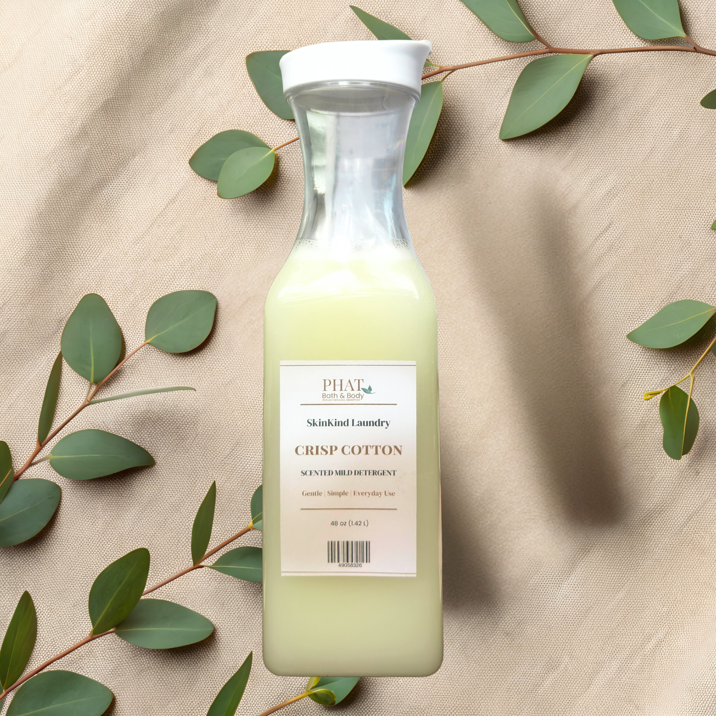 Bottle of SkinKind Laundry detergent byPHAT Bath & Body on a beige fabric background with green leaves.