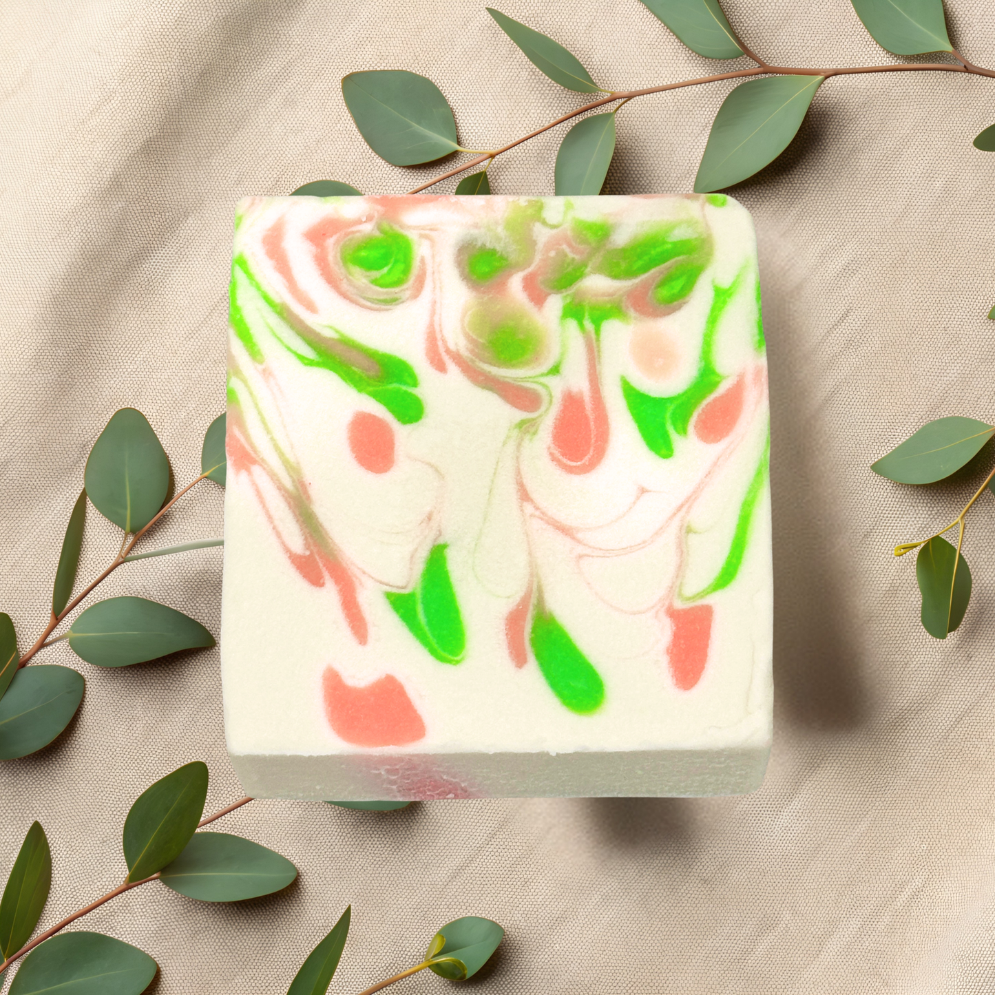 Bar of soap with green and pink swirls on a beige fabric background with eucalyptus leaves.