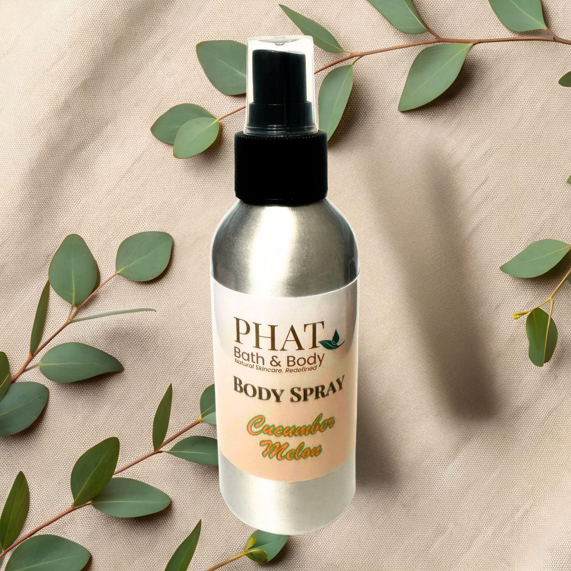 Body spray bottle labeled 'PHAT Bath & Body' on a beige fabric background with green leaves.