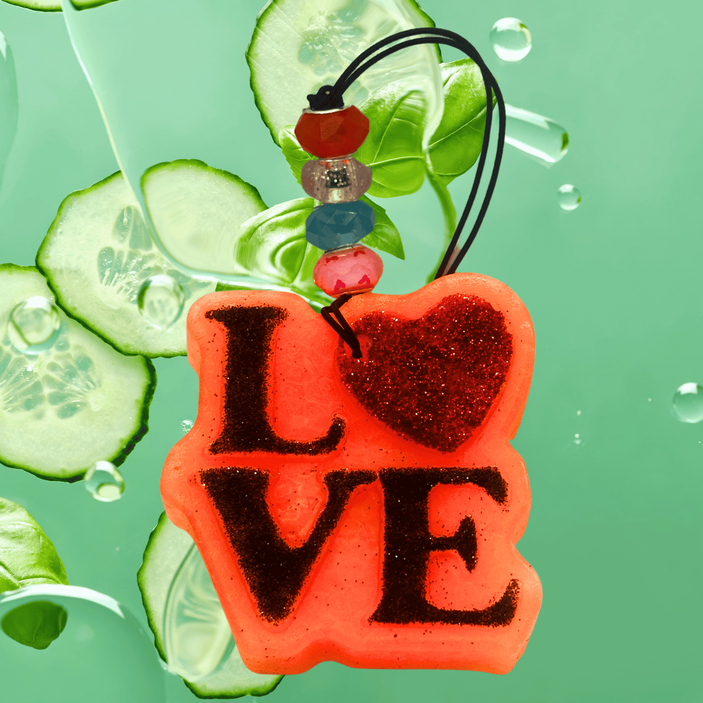 Red 'LOVE' charm with beads on a green background with cucumber slices