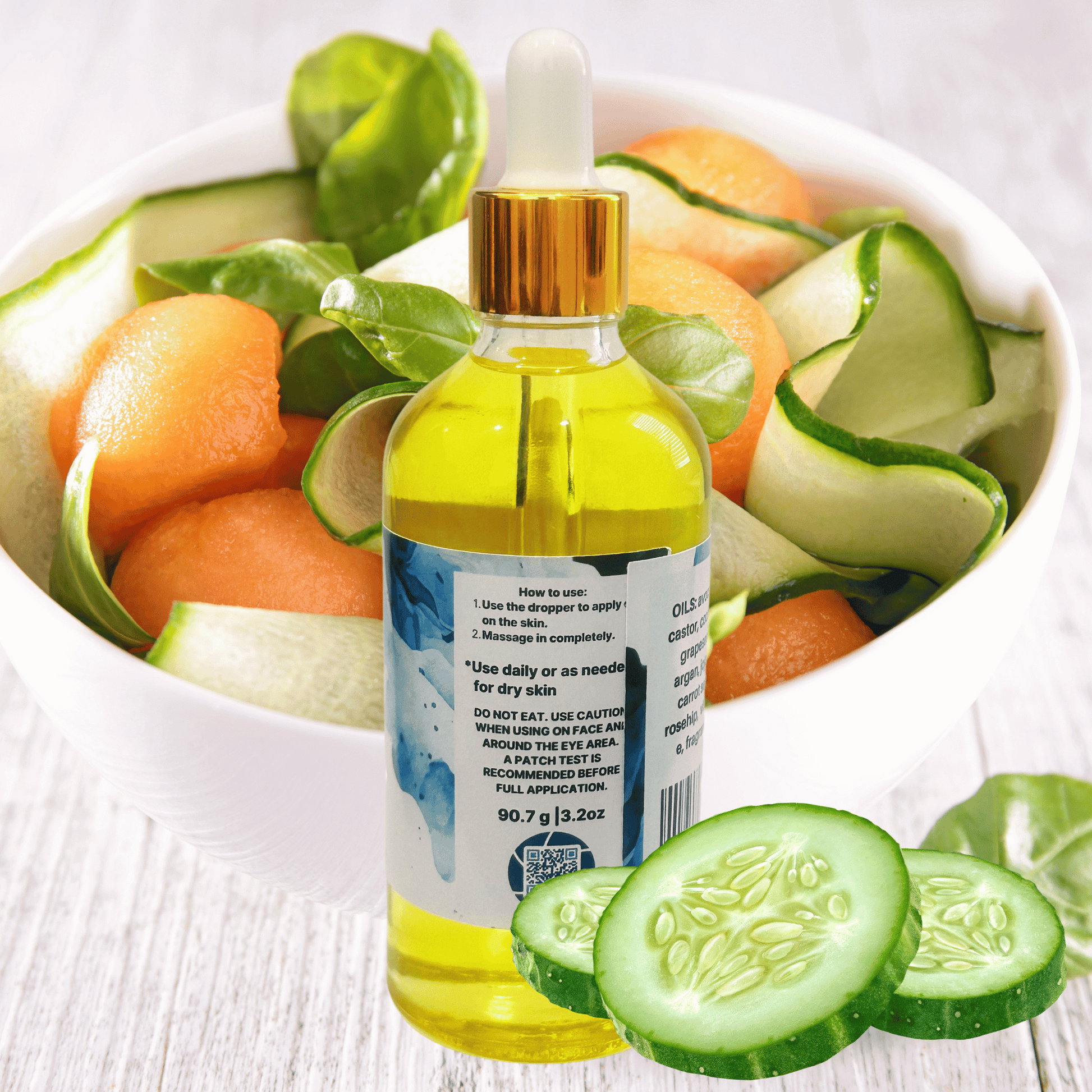 Bottle of body oil with a dropper surrounded by sliced cucumbers and melons on a white background
