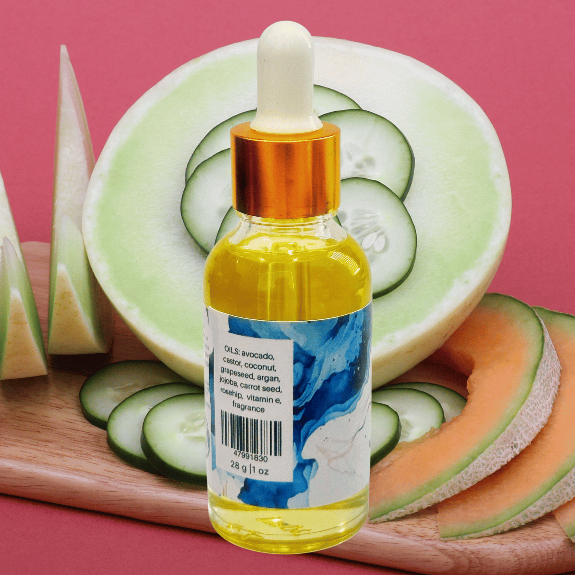 Bottle of oil with a dropper on a cutting board with sliced cucumbers, melon, and cantaloupe against a pink background