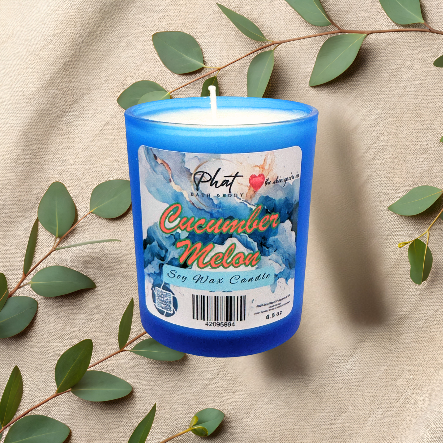 Blue candle labeled 'Cucumber Melon' with green leaves on a beige fabric background