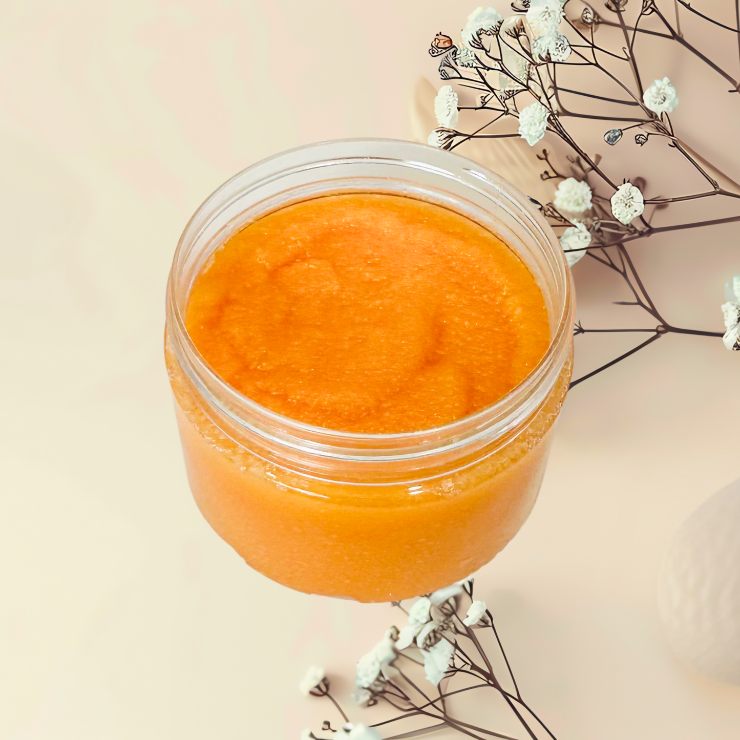 Jar of orange scrub with white flowers on a beige background