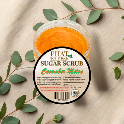 Jar of Phat Bath & Body Cucumber Melon sugar scrub with green leaves on a beige fabric background