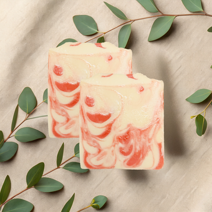 Two bars of pink and white marbled soap with green leaves on a beige fabric background