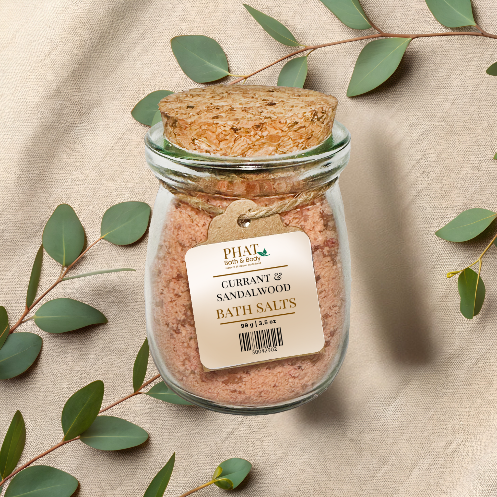 Jar of Currant and Sandalwood Bath Salts with a cork lid on a beige fabric background with eucalyptus leaves.