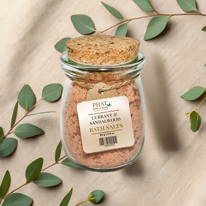 Jar of Currant and Sandalwood Bath Salts with a cork lid on a beige fabric background with eucalyptus leaves.
