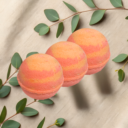 Three peach-colored bath bombs with green leaves on a beige fabric background