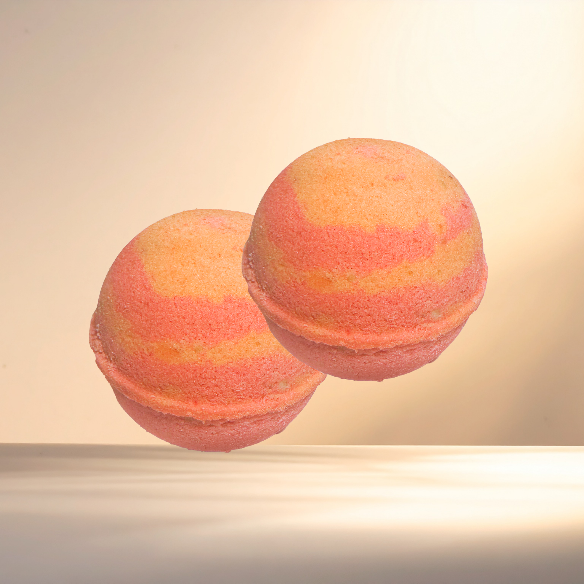 Two orange and pink bath bombs on a beige background
