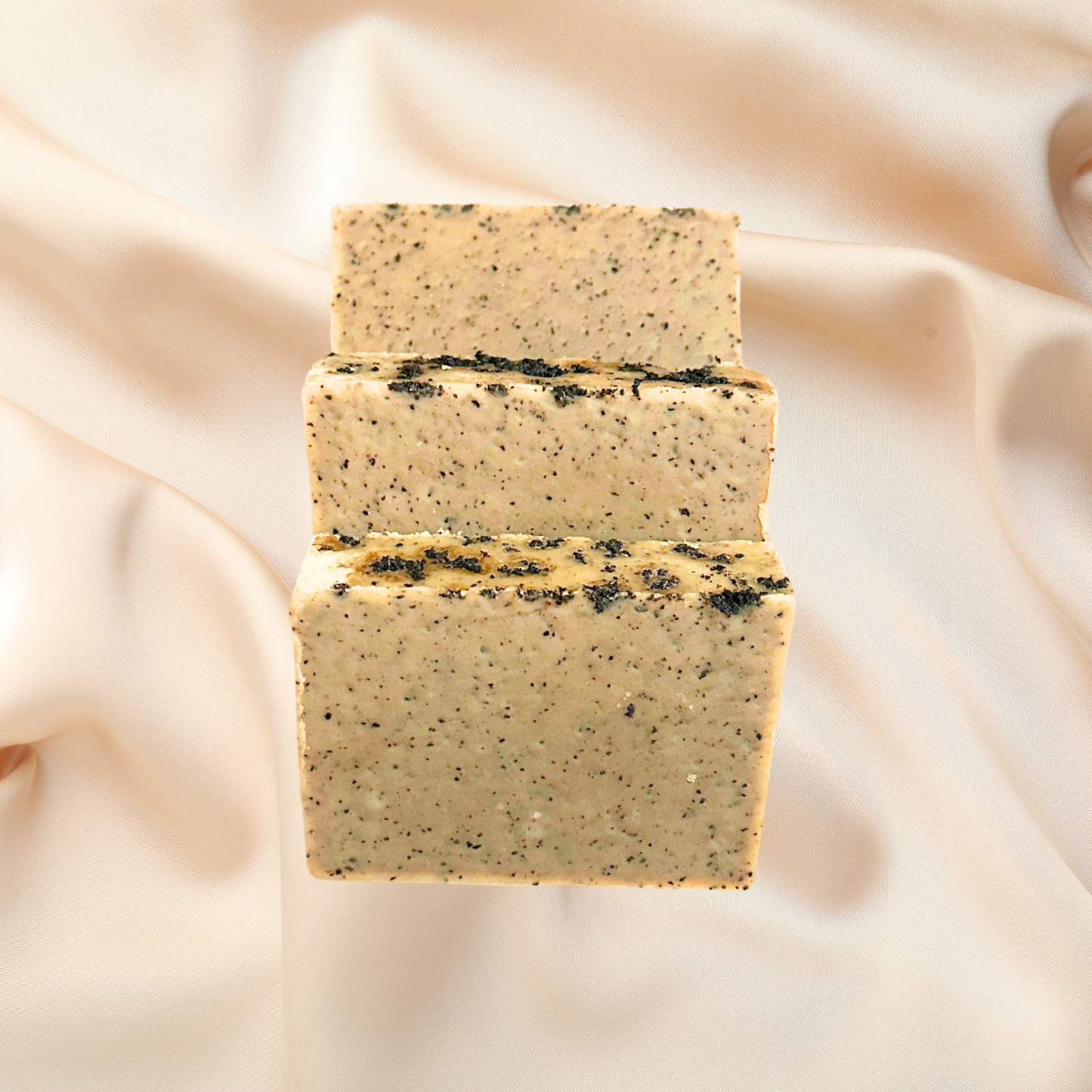 Three stacked soap bars with black specks on a beige fabric background