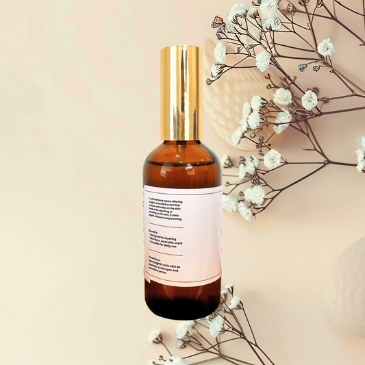 An amber glass bottle with a shiny gold cap and a white label, styled with dried white flowers on a soft beige background.
