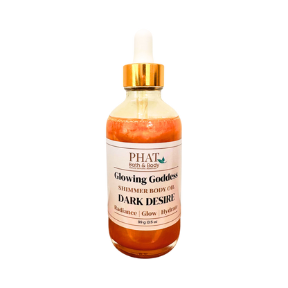 A glass bottle of PHAT Bath & Body 'Glowing Goddess' shimmer body oil in the 'Dark Desire' scent, featuring an amber-colored liquid, a white label, and a gold collar with a white dropper cap, set against a plain white background.