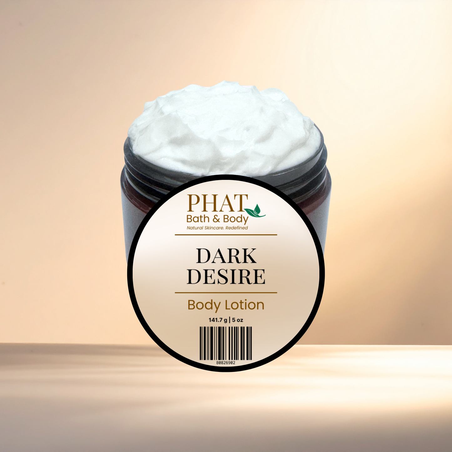 A jar of PHAT Bath & Body 'Dark Desire' body lotion, showing the white whipped lotion inside a dark jar with a large circular label in front, set against a warm beige gradient background.