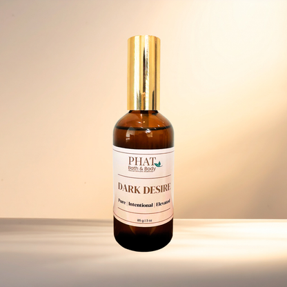 An amber glass bottle of PHAT Bath & Body 'Dark Desire' pure intentional scented  with a shiny gold cap, set against a warm beige background.