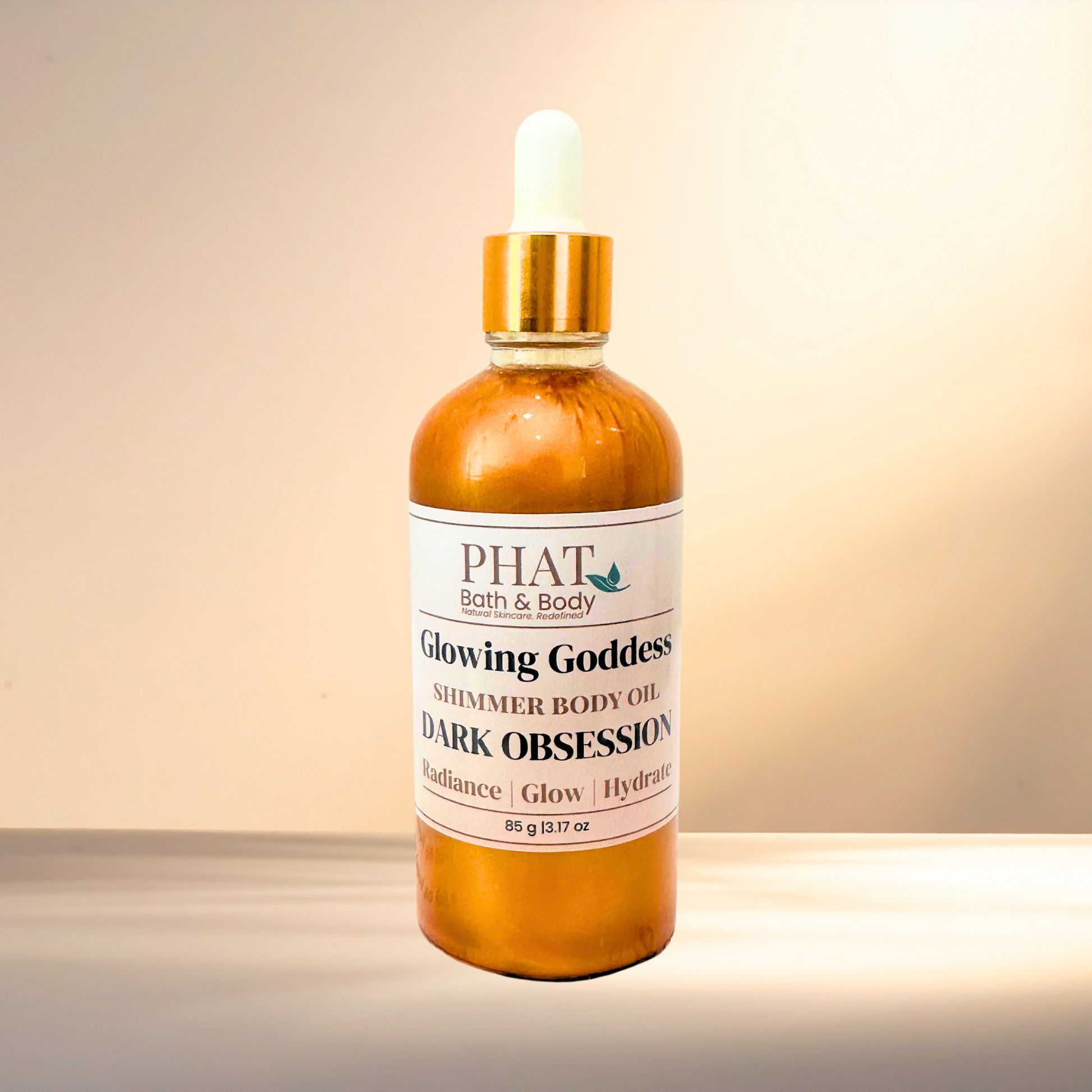 Bottle of 'Glowing Goddess' shimmer body oil by PHAT Bath & Body on a gradient background