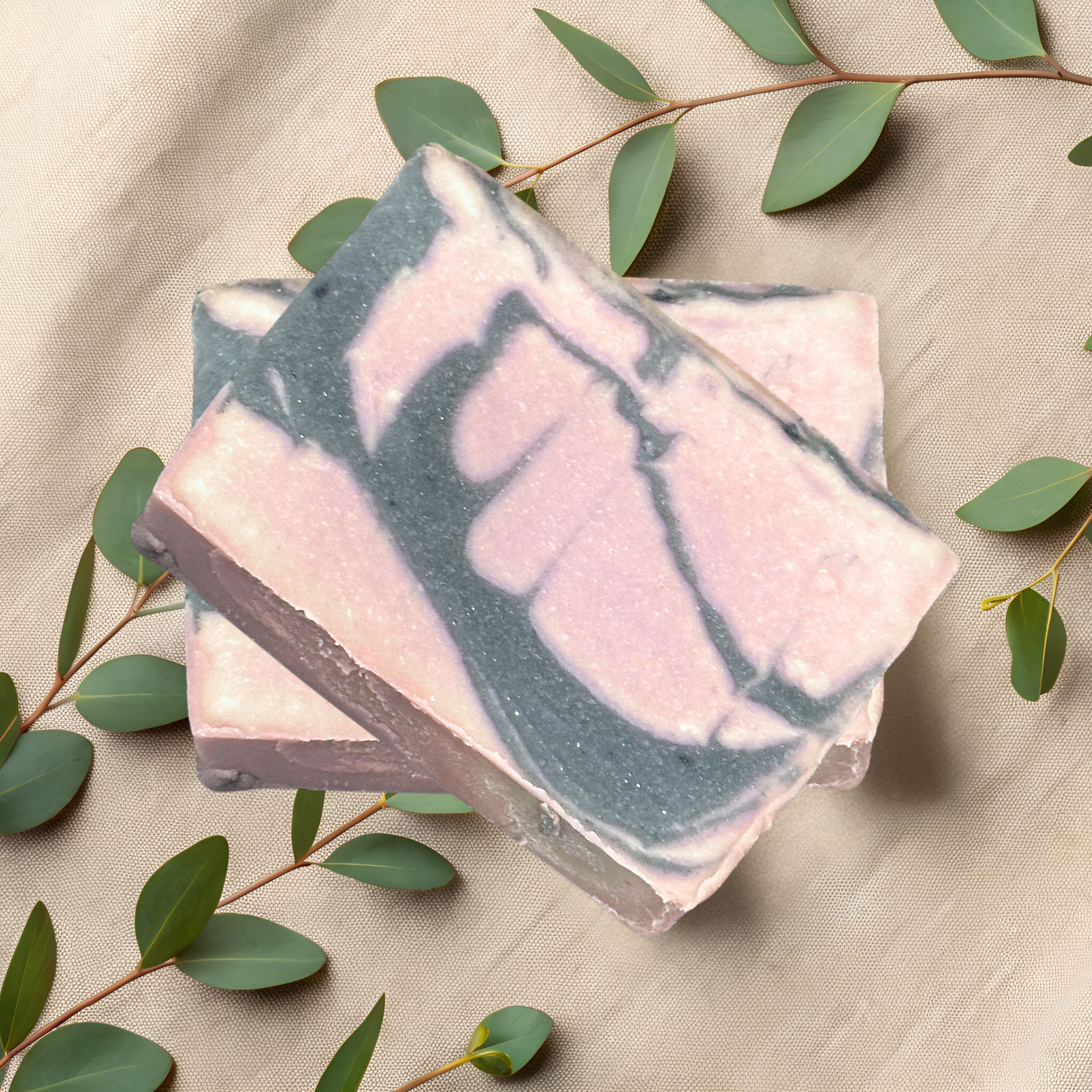 Two bars of soap with a marbled pattern on a beige fabric background with green leaves.