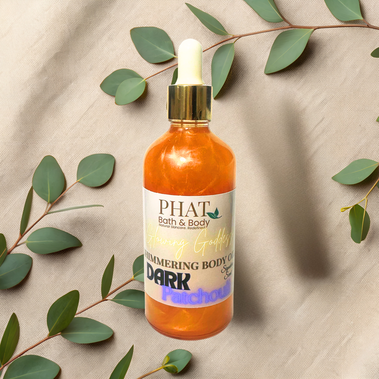 Bottle of 'PHAT Bath & Body' shimmering body oil with green leaves on a beige fabric background