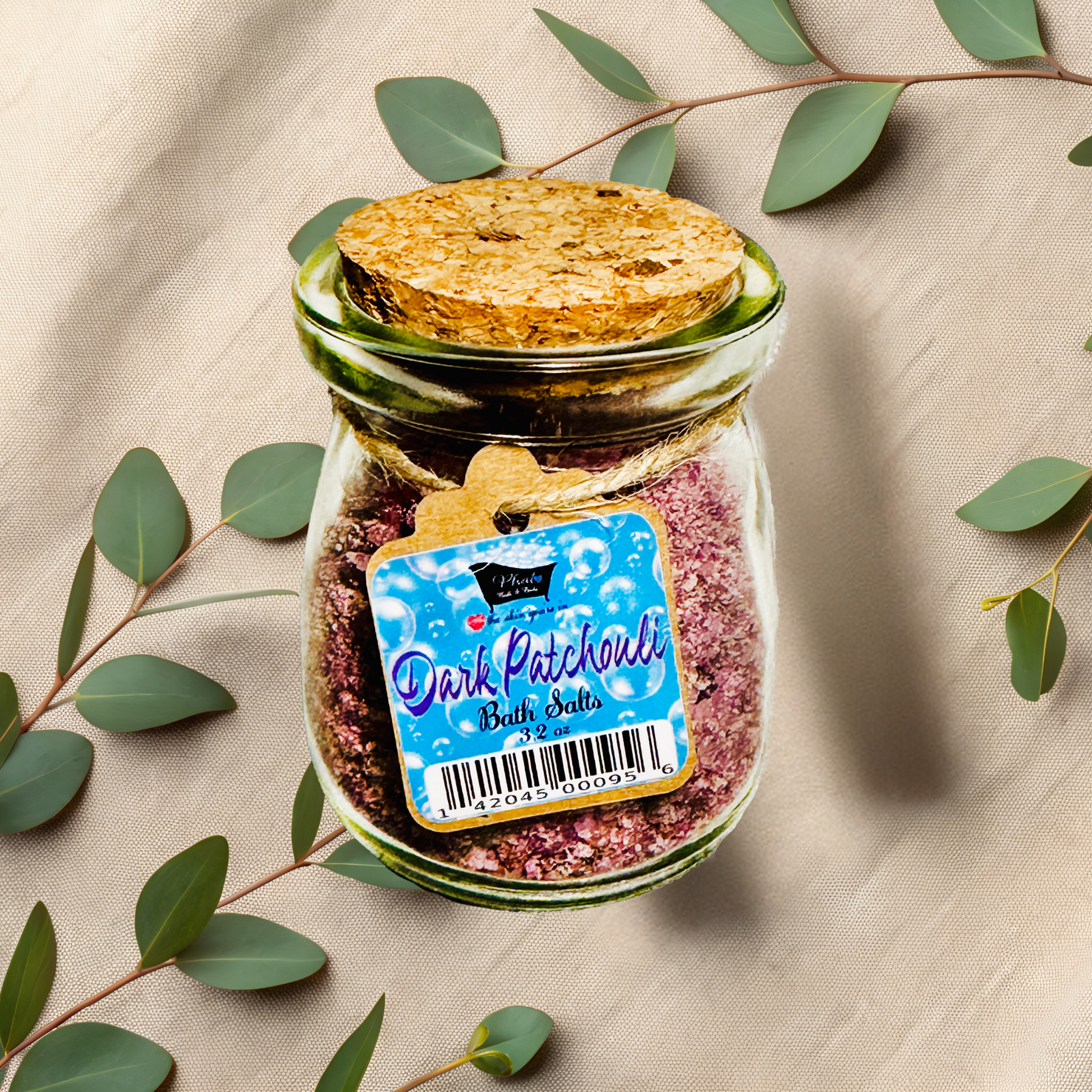 Jar of 'Dark Patchouli' bath salts with a label on a beige fabric background with green leaves.