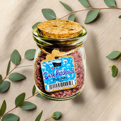 Jar of 'Dark Patchouli' bath salts with a label on a beige fabric background with green leaves.