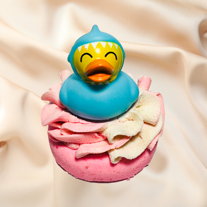 Colorful bath bomb with a blue rubber duck on top against a beige fabric background