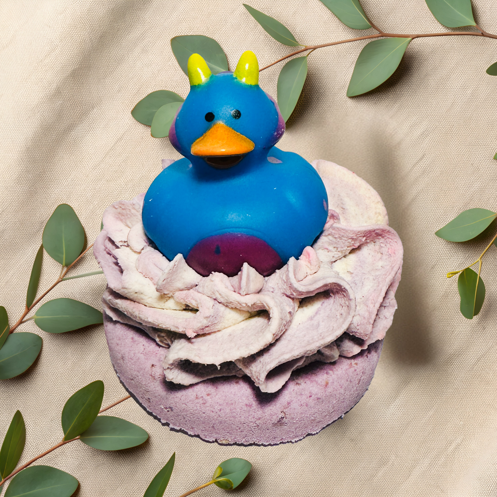Blue rubber duck on a purple bath bomb with frosting and green leaves on a beige fabric background