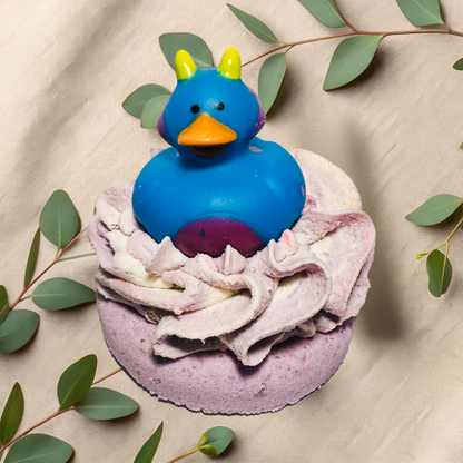 Blue rubber duck on a purple bath bomb with frosting and green leaves on a beige fabric background