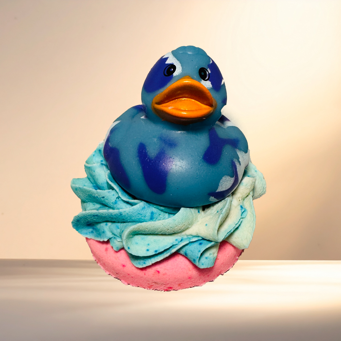 Blue rubber duck on top of a bubble bomb with white and blue frosting against a beige background