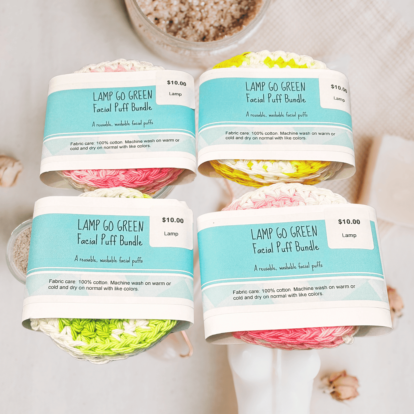 Four colorful facial scrubbies with labels on a pink textured background