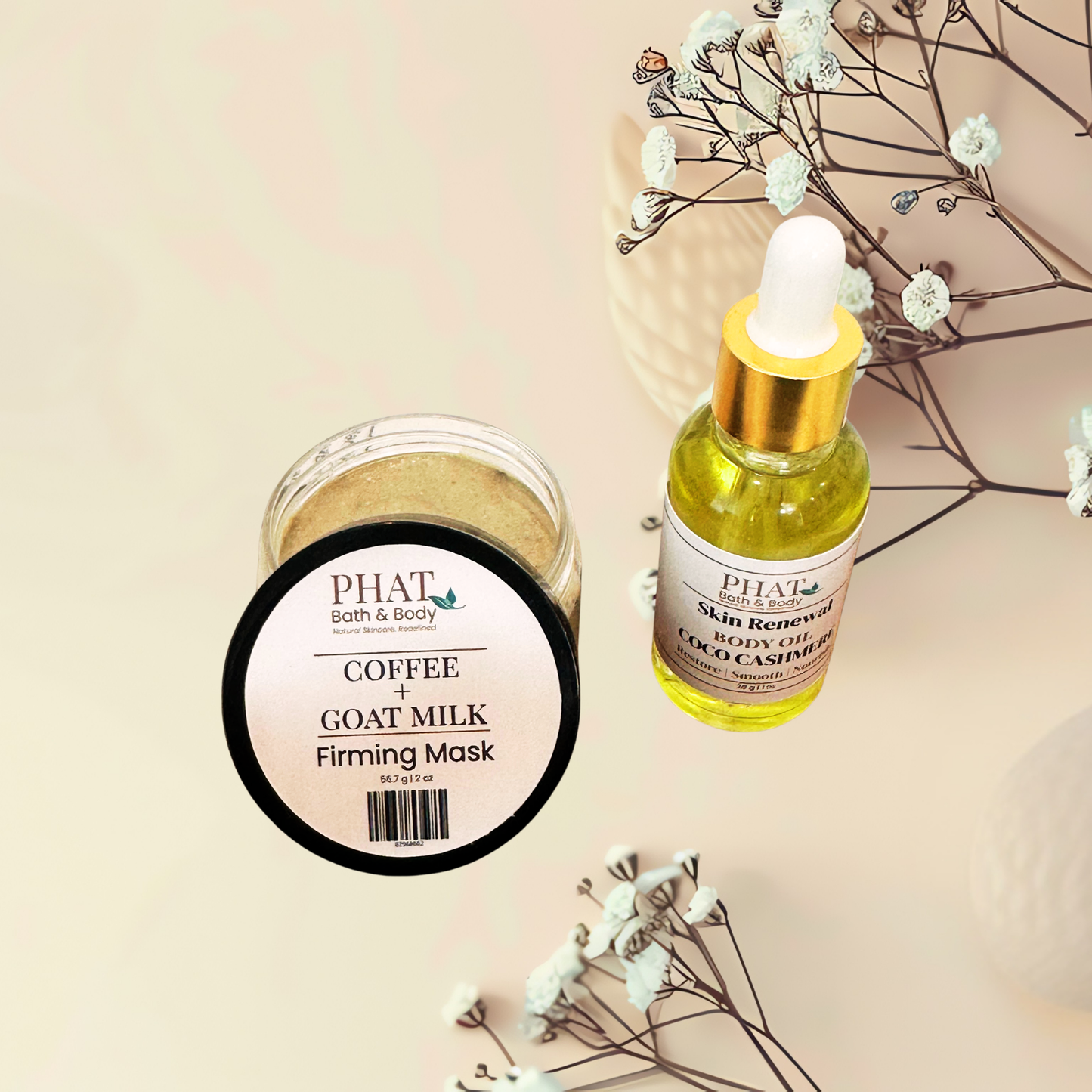 Two PHAT bath & body products arranged on a warm beige background with dried floral stems: a clear jar of Coffee + Goat Milk Firming Mask and a small dropper bottle of Gold-Skin Renewal Body Oil.