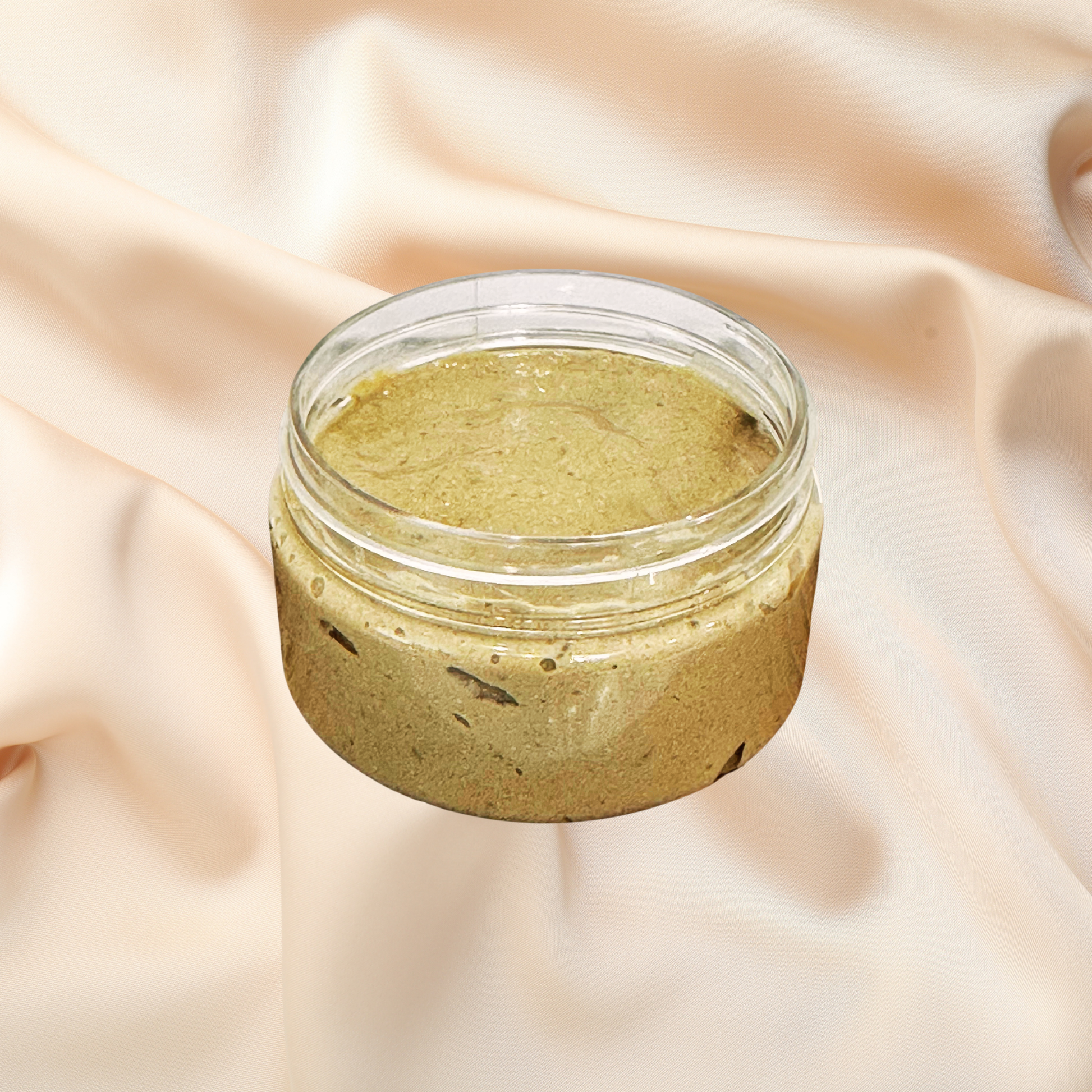 An open clear cosmetic jar filled with a textured olive-green mask, set against a draped beige fabric background.