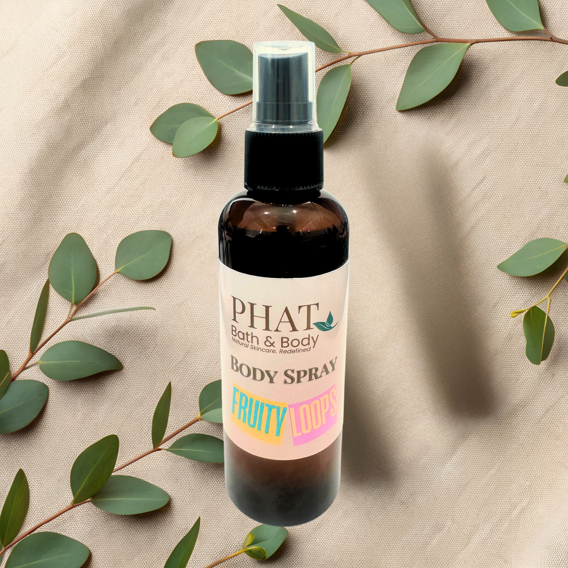 Body spray bottle with 'Phat Bath & Body' label on a beige fabric background with green leaves.