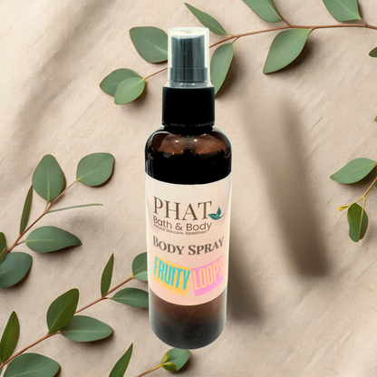 Body spray bottle with 'Phat Bath & Body' label on a beige fabric background with green leaves.