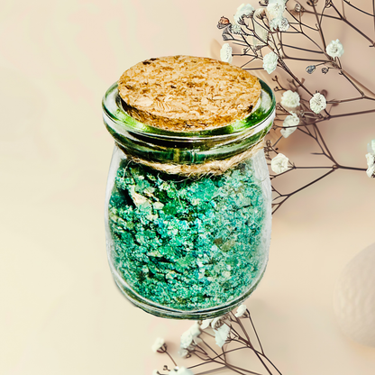Glass jar with cork lid containing green bath salts, surrounded by dried flowers on a beige background