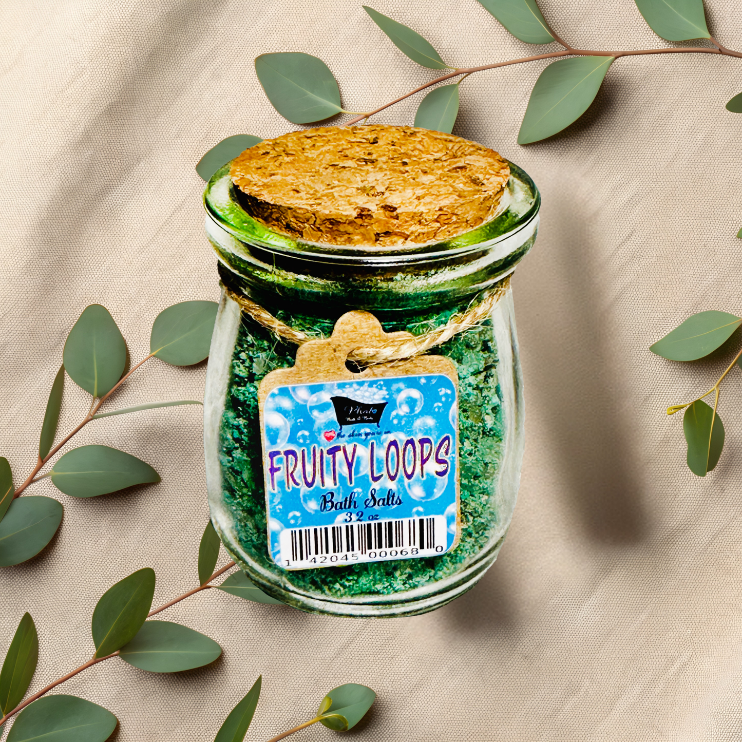 Jar of Fruity Loops bath salts with a decorative label on a beige fabric background with green leaves.
