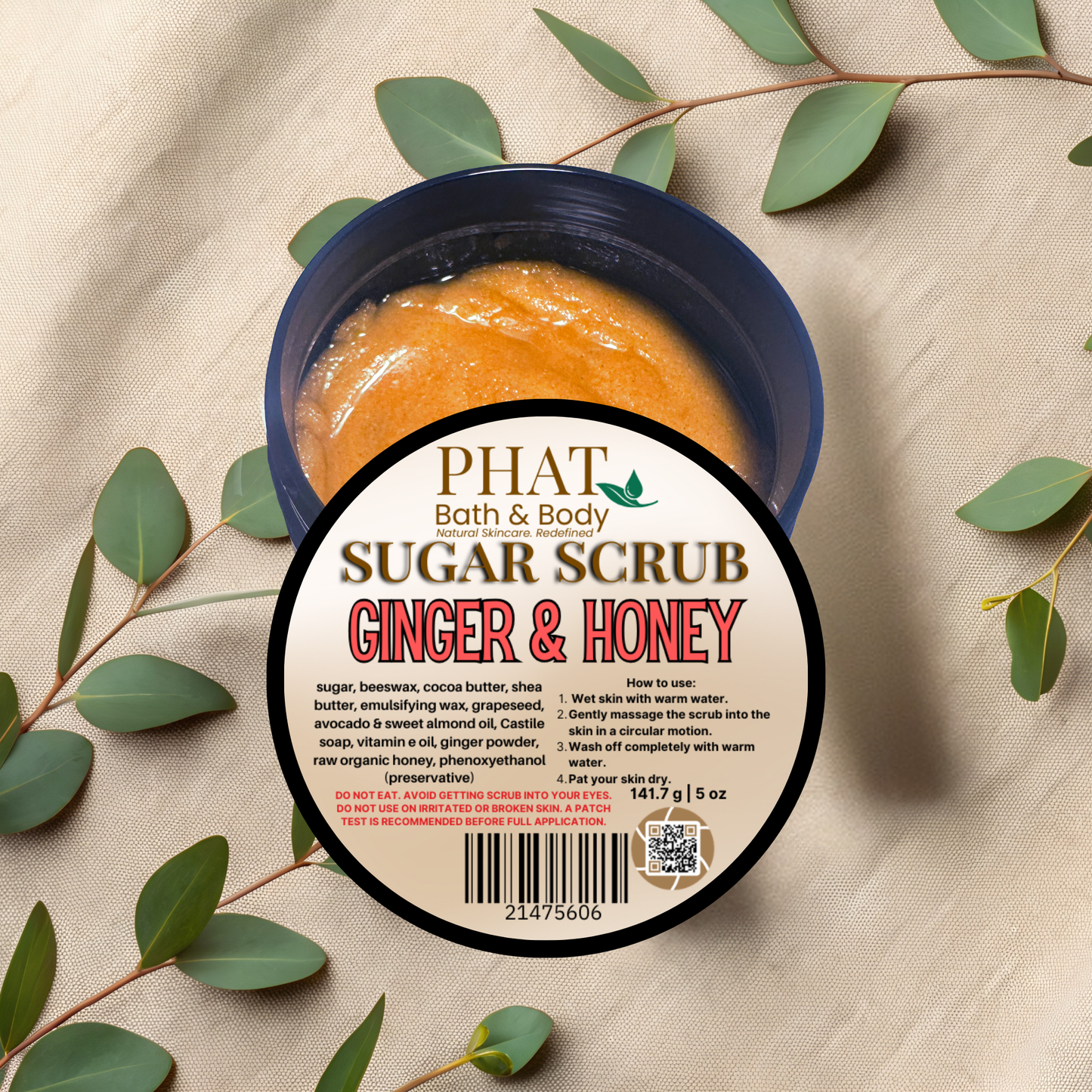Ginger & Honey sugar scrub container with leaves on a beige fabric background