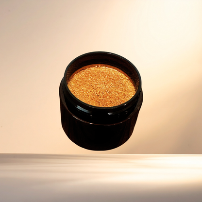 A small open black cosmetic jar filled with shimmering bronze powder, photographed against a warm beige studio background with a reflective surface below.